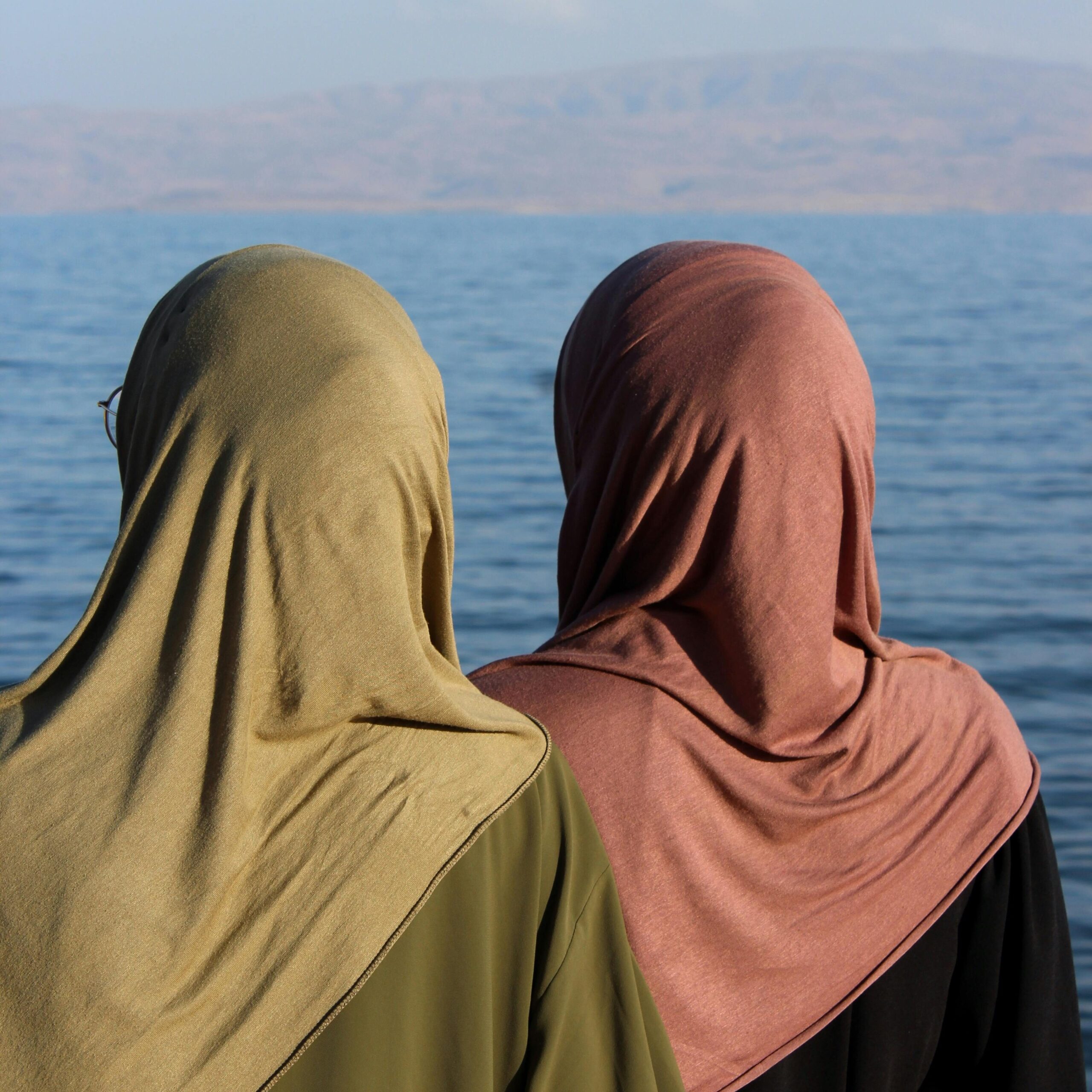 Back view of two women in hijabs standing by the sea, capturing a peaceful moment.